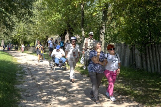 Uczestnicy Mazowieckiego Dnia Integracji Osób z Niepełnosprawnościami idący dróżką wśród chat skansenu.