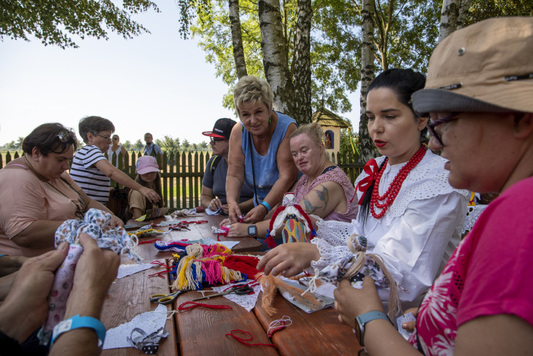 Gupa ludzi siedząca przy stole i tworząca lalki motanki.