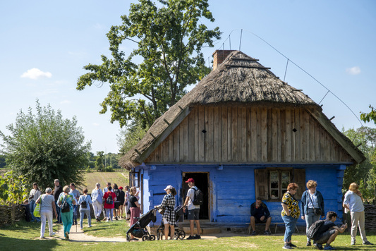 Grupa ludzi zmierzająca na pokaz w jednej z wiejskich chat skansenu.