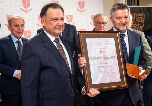 Grupa mężczyzn w garniturach, dwóch z przodu trzyma ramkę z certyfikatem. 