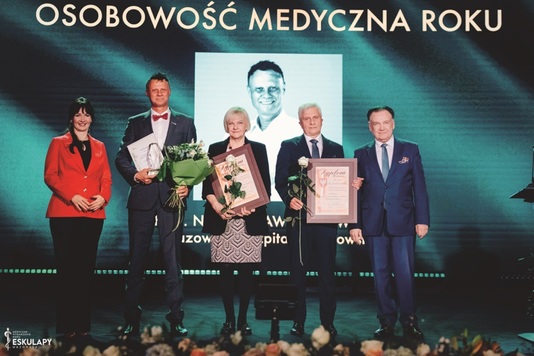 Nagrodzony dr hab. n. med. Paweł Skowronek,  konsultant wojewódzki w dziedzinie Ortopedii i Traumatologii Narządu Ruchu w Mazowieckim Szpitalu Bródnowskim Sp. z o. o. Stoi na scenie otoczony kilkoma osobami.