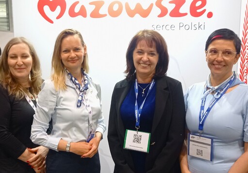 Cztery kobiety uśmiechają się do kamery na tle napisu 