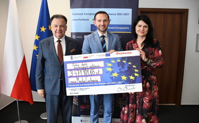 Trzy osoby trzymają duży symboliczny czek na kwotę 3 471 101,65 zł. W tle flagi Polski i Unii Europejskiej oraz baner z napisem "Fundusze Europejskie dla Mazowsza 2021-2027".